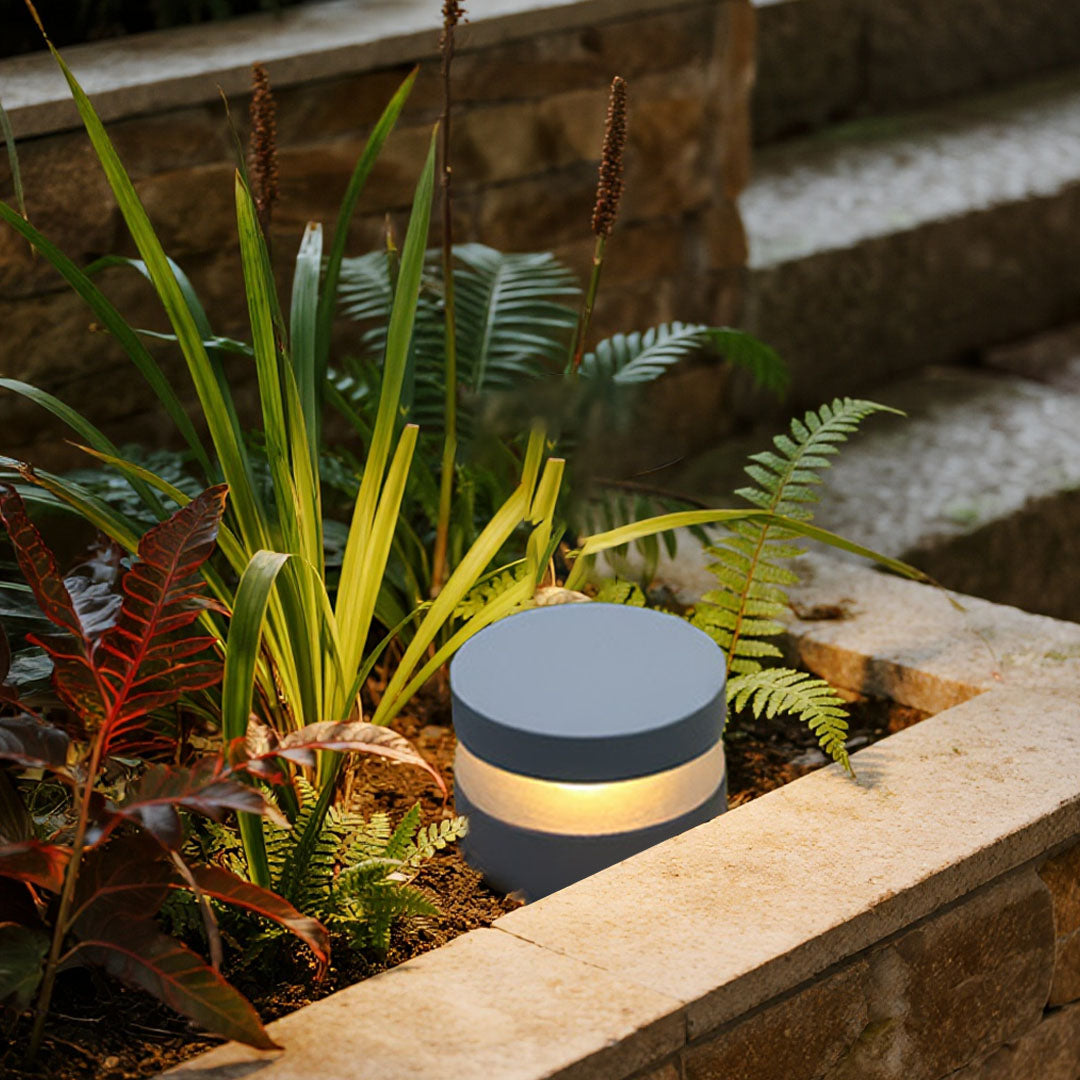 Modern 110v landscape lights installed along a raised garden bed, providing soft warm illumination for plants and stone edges.