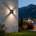 Architectural black outdoor sconce light featuring glass shade chandelier styling creating four-way light spread on stone wall.