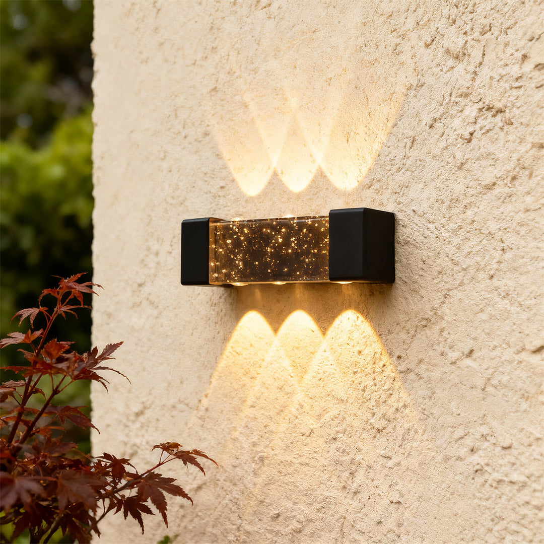 Architectural up down wall light featuring glass shade chandelier styling providing warm uplighting and downlighting on textured stone.