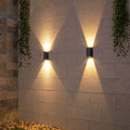 Modern black outdoor light producing brilliant warm illumination against rich textured wall