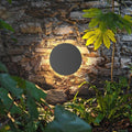 Round backlit wall light on stone wall in garden