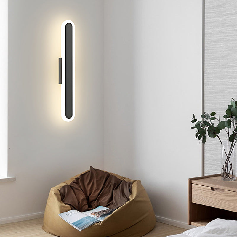 Bar wall light with a vertical design, illuminating a modern living room with a beige armchair.