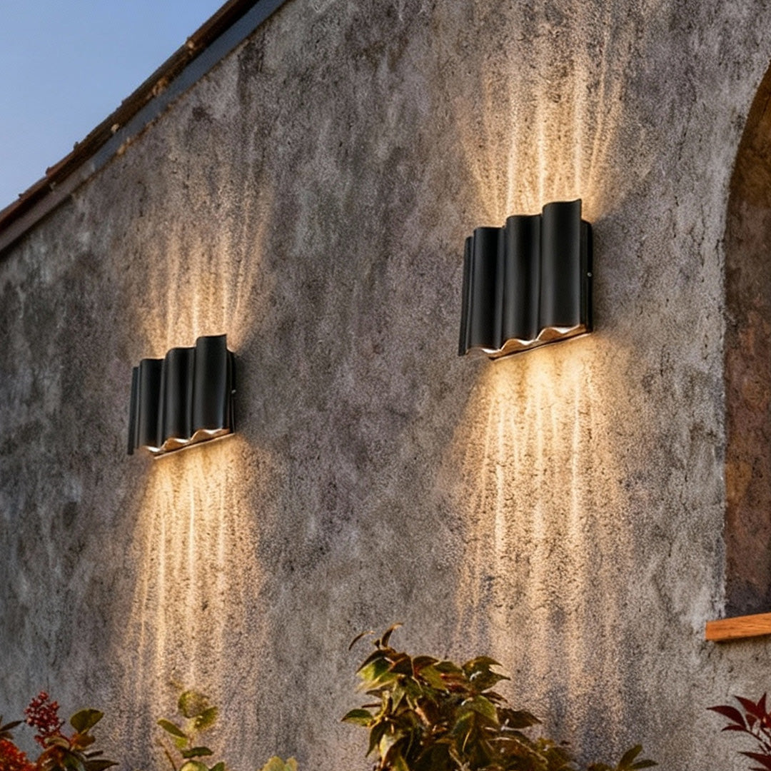 Black beam wall light installed on a gray exterior wall, casting upward light beams.