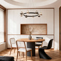 Black and gold modern chandelier suspended above dining table in minimalist space with wooden chairs and neutral tones
