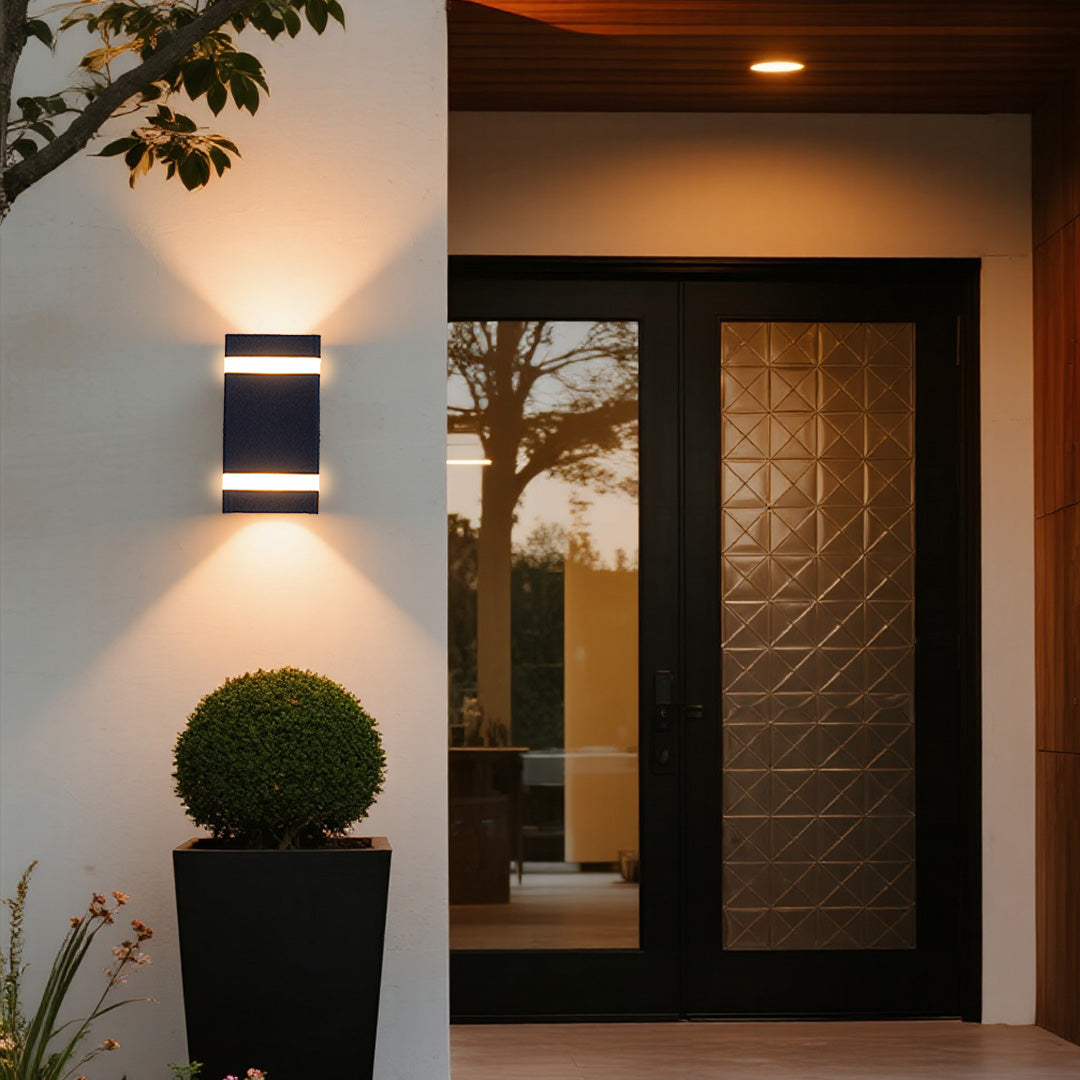 Black garden wall light with white stripe accent mounted on white wall beside entrance