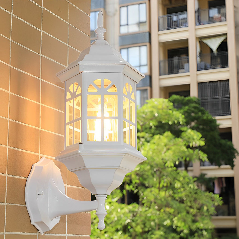 Black outdoor lantern sconce casting a gentle glow near a green garden.