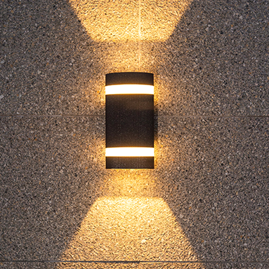 Black rectangular garden wall light creating warm glow on textured stone surface at night