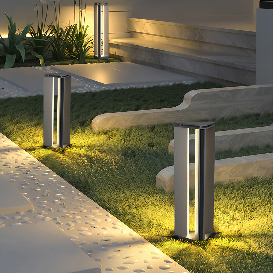 Warm-lit bollard outdoor lights placed along a landscaped garden path creating soft ambient illumination.