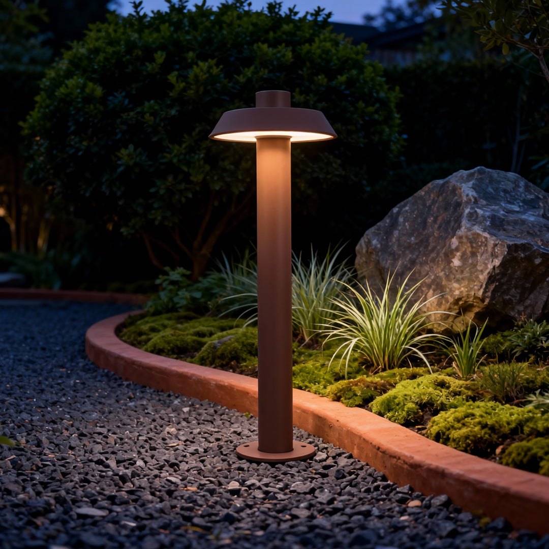 Warm bronze aluminum path lights lighting up a landscaped outdoor scene with stones and greenery.
