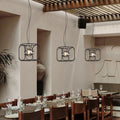 Caged pendant light hanging above a modern dining area, featuring a black metal cage design with warm ambient lighting.