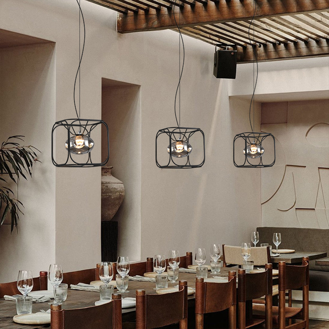 Caged pendant light hanging above a modern dining area, featuring a black metal cage design with warm ambient lighting.