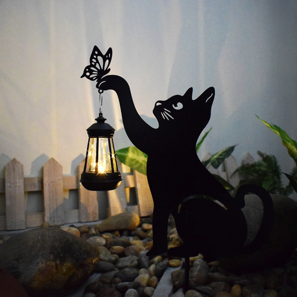 Cat silhouette light casting a gentle glow near a garden bed.