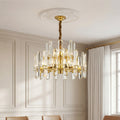 Striking chandelier brass modern design featuring staggered clear crystal prisms and a gold frame suspended from a decorative ceiling medallion.
