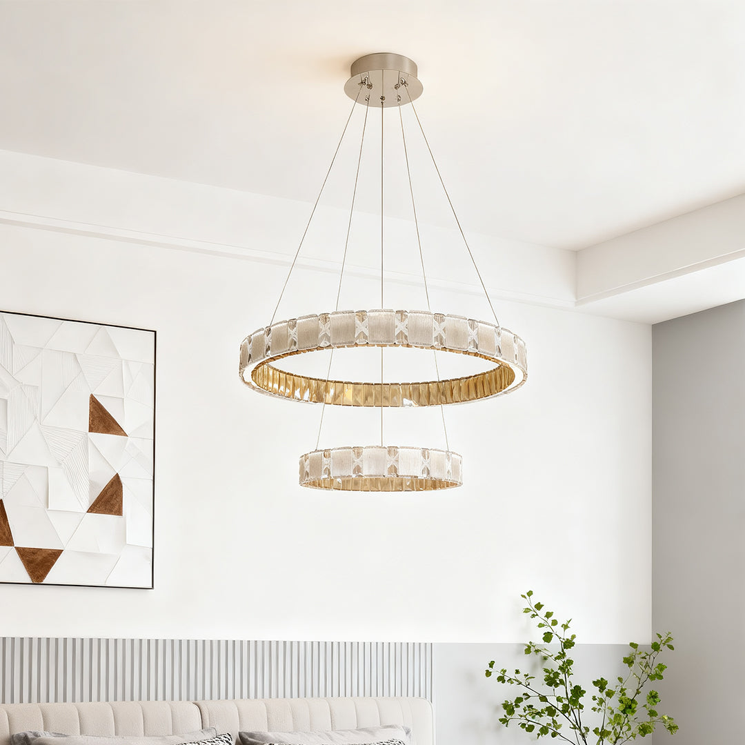 Circular chrome chandelier suspended in minimalist white interior with pendant cable design.