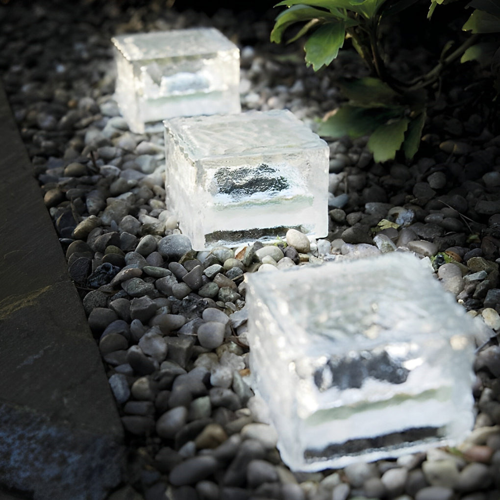 Clear ice cube pathway lights arranged in a row on gravel ground.