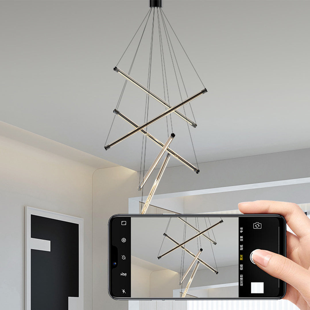 Close up of a LED linear chandelier showcasing gold bars and cables, photographed by a hand holding a smartphone.