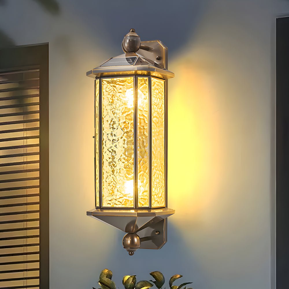 Copper outdoor wall lantern with hammered glass panels, casting a warm glow on a modern exterior wall at night.