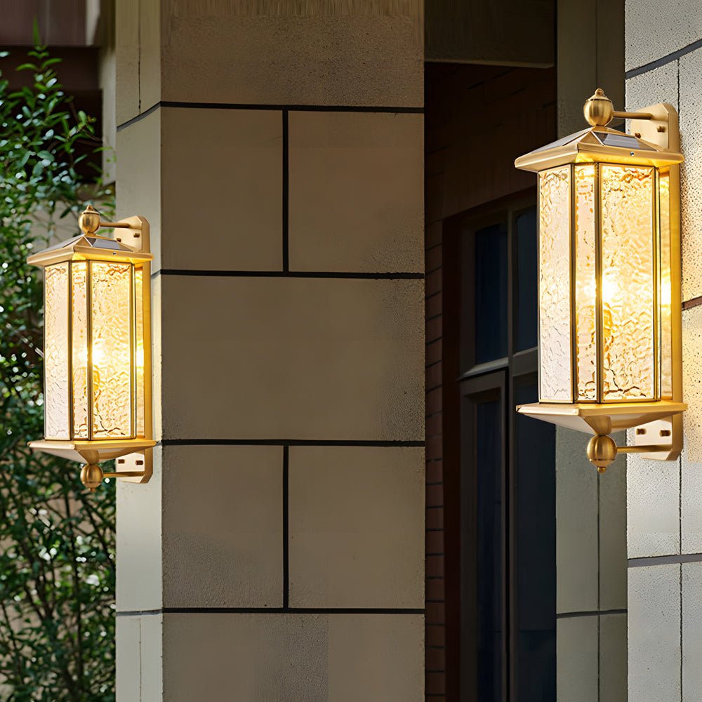 Copper outdoor wall lantern mounted on a stone wall near greenery, blending classic metalwork with natural surroundings.