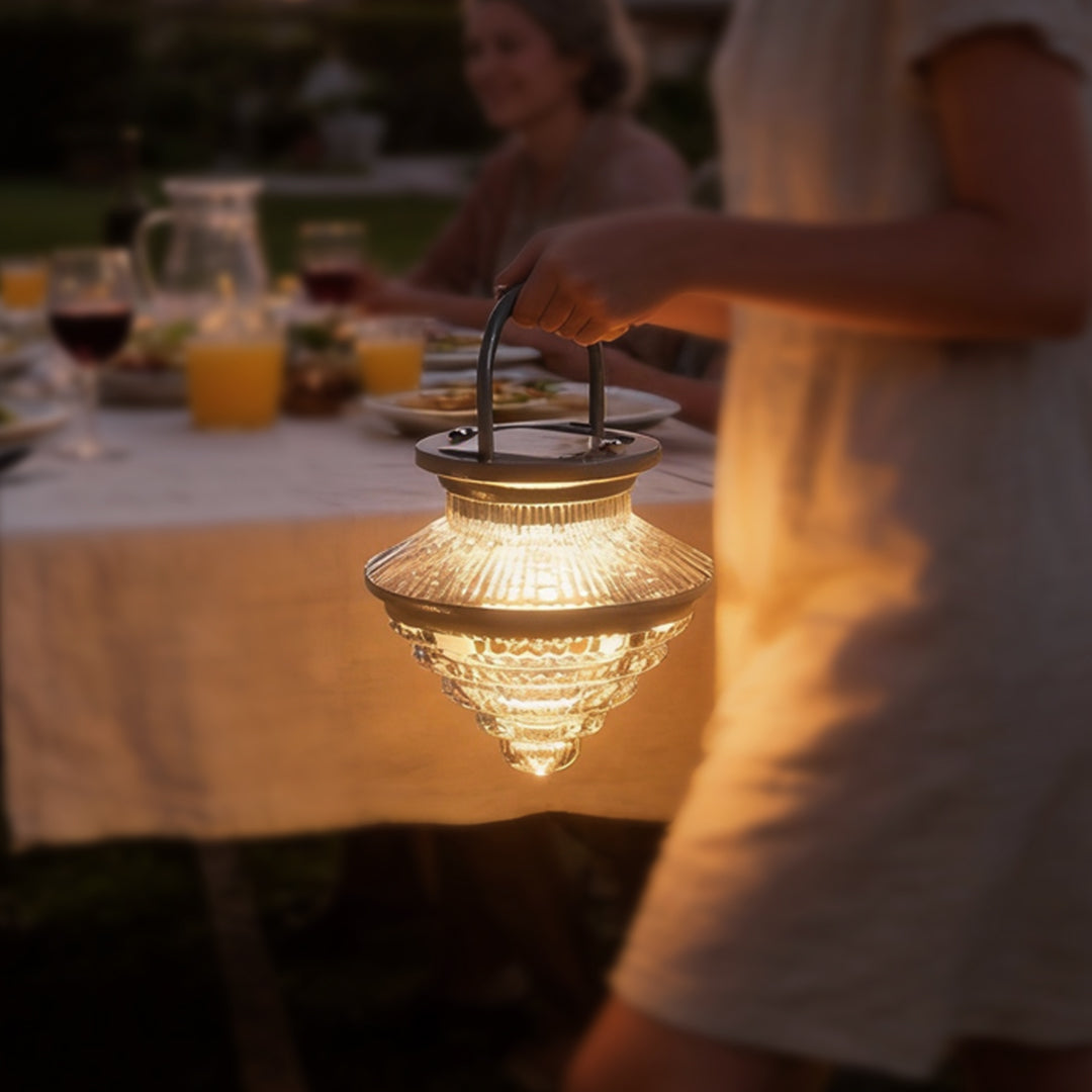 Cordless acrylic hanging lantern carried by hand during an outdoor dinner, offering portable and elegant lighting.