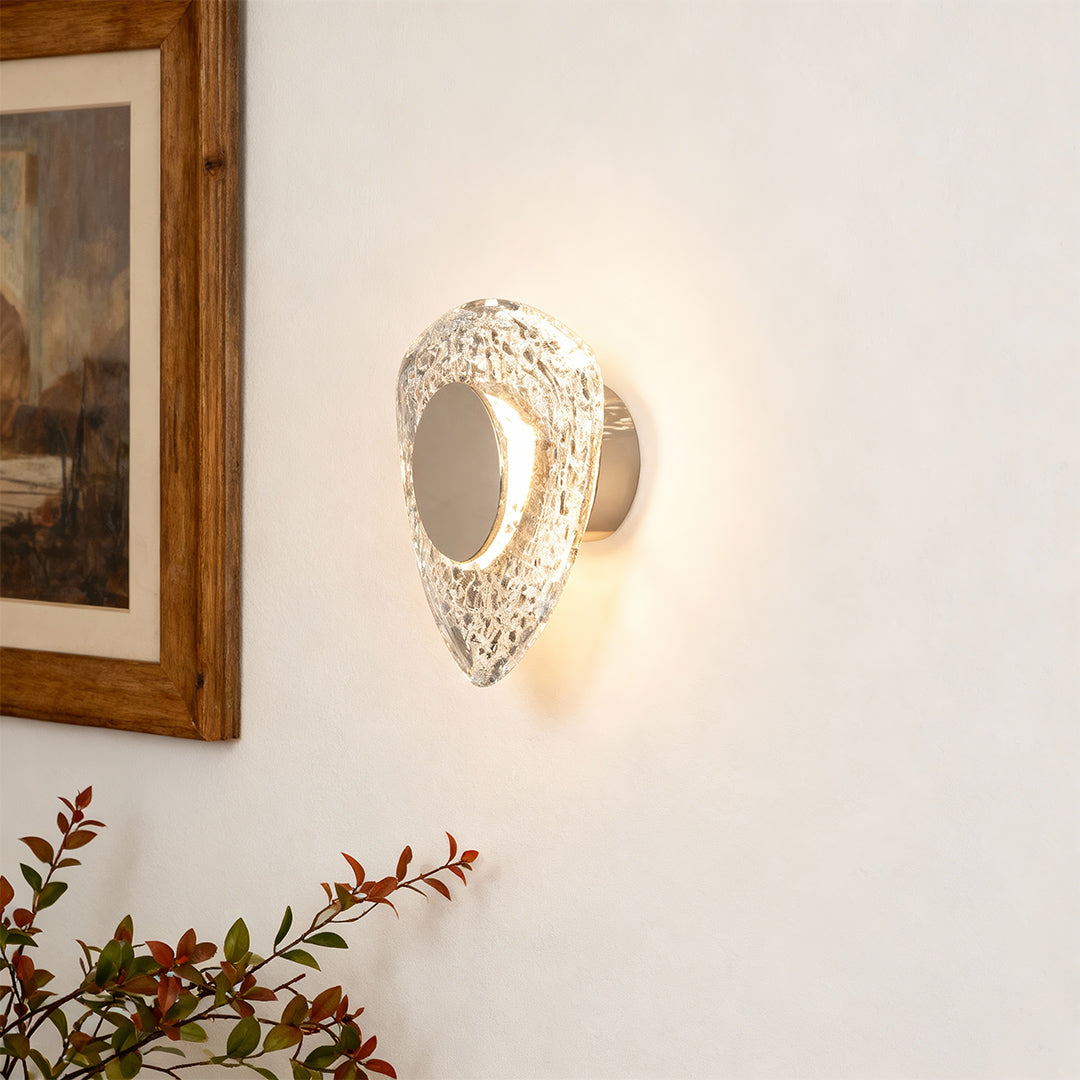 Crystal wall sconce light fixture creating warm ambiance beside wooden framed mirror with autumn foliage decor