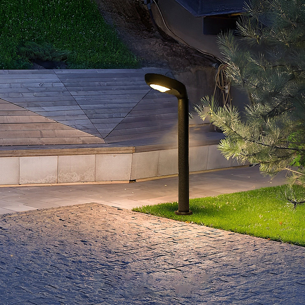 Curved bollard light illuminating a stone path in a landscaped yard.