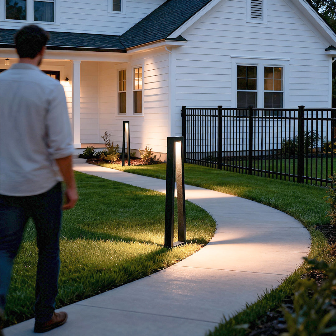 Soft warm outdoor lighting for landscaping along a curved walkway near a home using tall bollard lights.