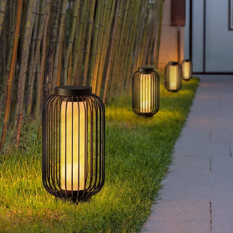 Lantern metal outdoor light with cylindrical shape, positioned on grass for elegant and warm outdoor ambiance.