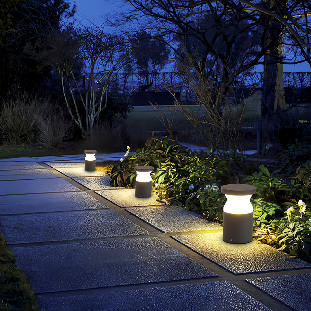 Line of short, cylindrical modern path lights with glowing white diffusers illuminating a flagstone walkway at night.