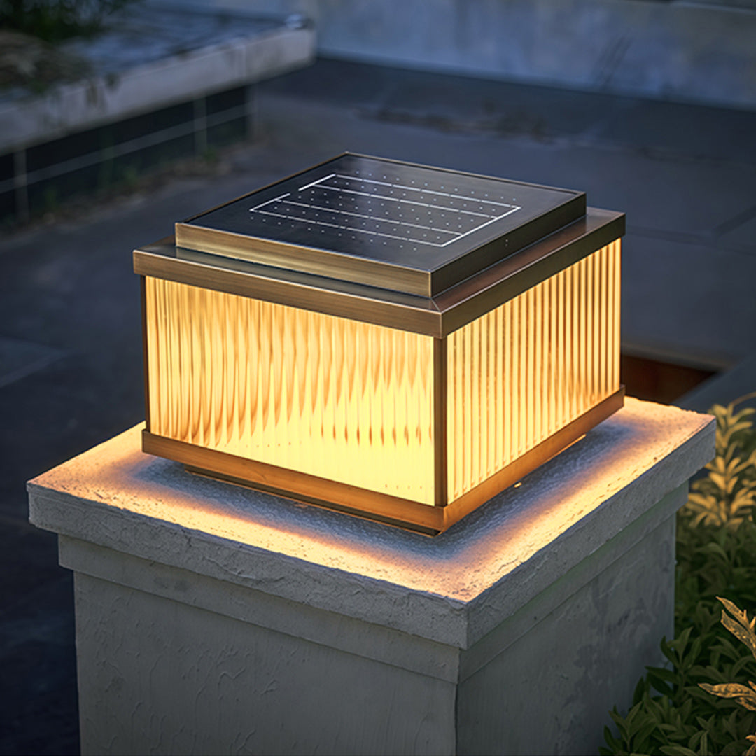 Warm-lit copper pillar light mounted on wooden deck post with natural outdoor garden backdrop.