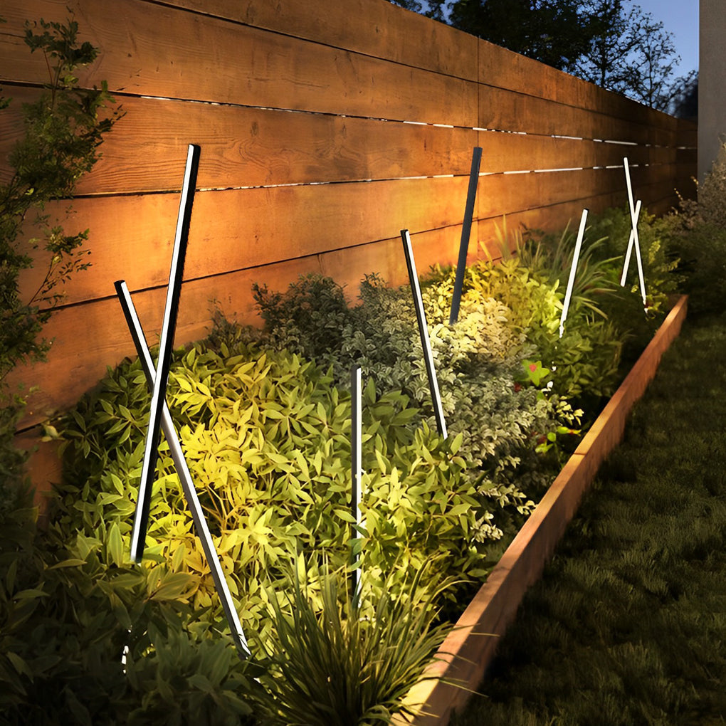 Angled decorative contemporary outdoor floor lamps highlighting landscape plants and wooden fencing.