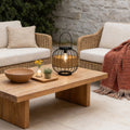 Decorative hanging solar lantern with a wicker design, placed on an outdoor coffee table setting.