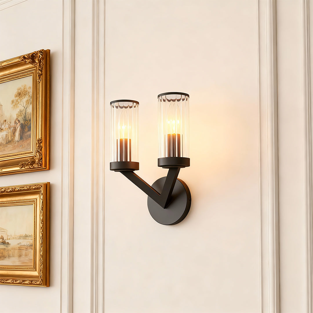 Double sconce wall light illuminating elegant hallway with ornate gold-framed mirror.