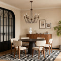 Elegant French style chandelier with an antique bronze finish and scrolling arms, hanging above a contemporary round dining table.