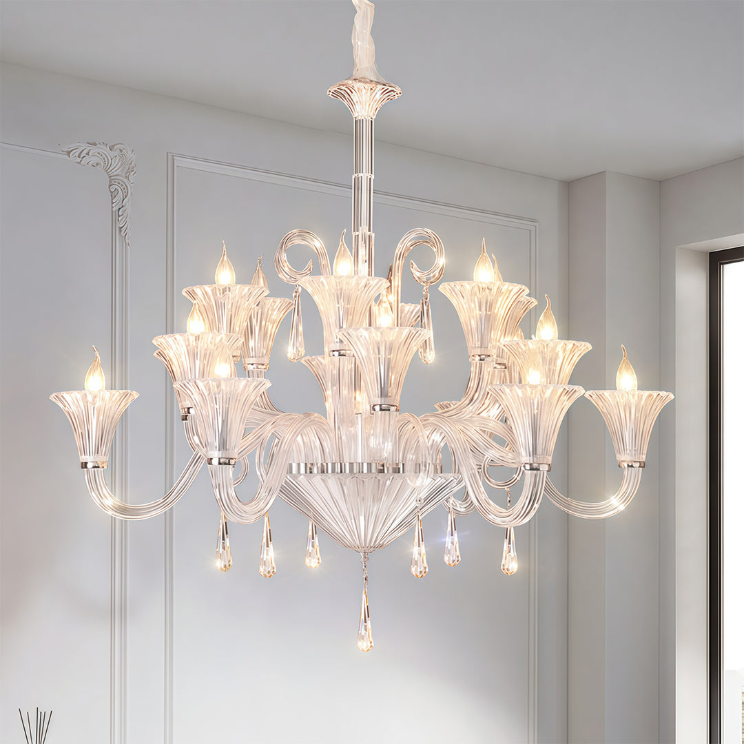 Elegant art glass chandelier suspended in minimalist white bedroom with soft grey bedding and natural light.