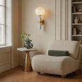 Elegant gold wall sconce lighting with a white globe shade in a cozy modern reading corner.