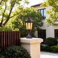 Elegant residential pillar light mounted on beige pillar near modern gate with trees and greenery