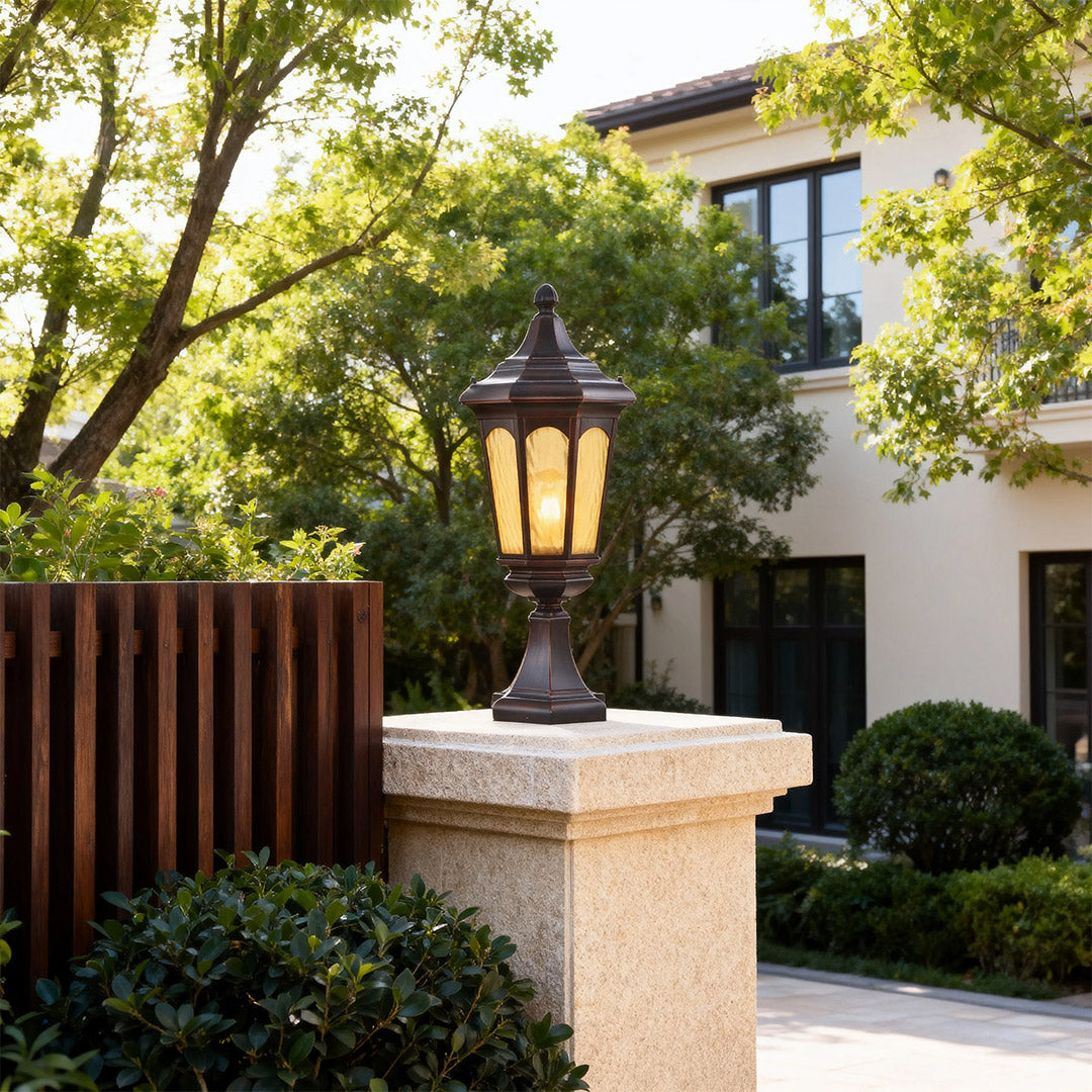 Elegant residential pillar light mounted on beige pillar near modern gate with trees and greenery