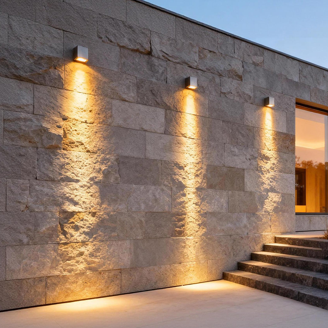 Facade spot lights installed on a modern stone exterior wall, casting warm vertical beams that highlight architectural texture.
