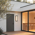Fan shaped wall sconce with a modern design, illuminating a contemporary house entrance at night.