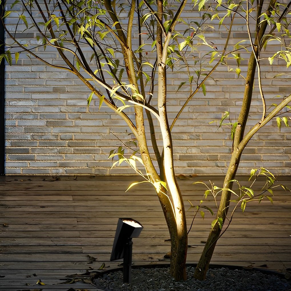 Flood spike light illuminating small tree on wooden deck with soft warm light for cozy outdoor atmosphere.