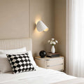 Folding wall sconce illuminating a modern bedroom with warm ambient glow.