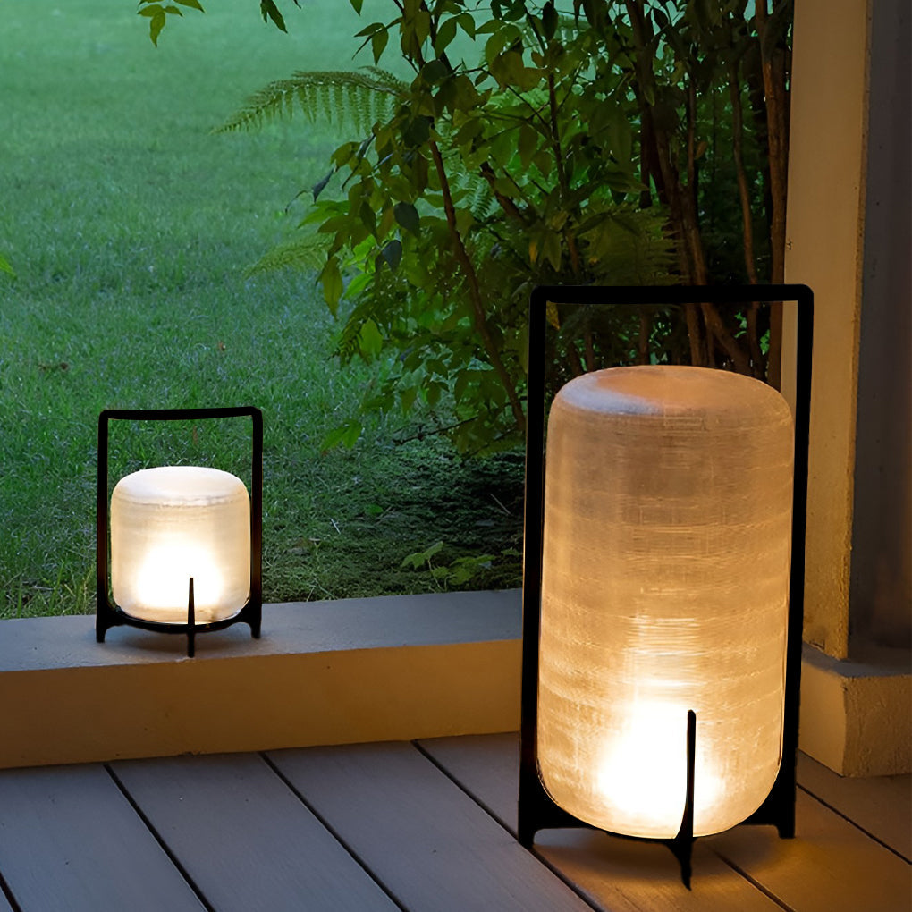 Outdoor modern handle lantern with frosted glass shade on wooden deck beside open book.