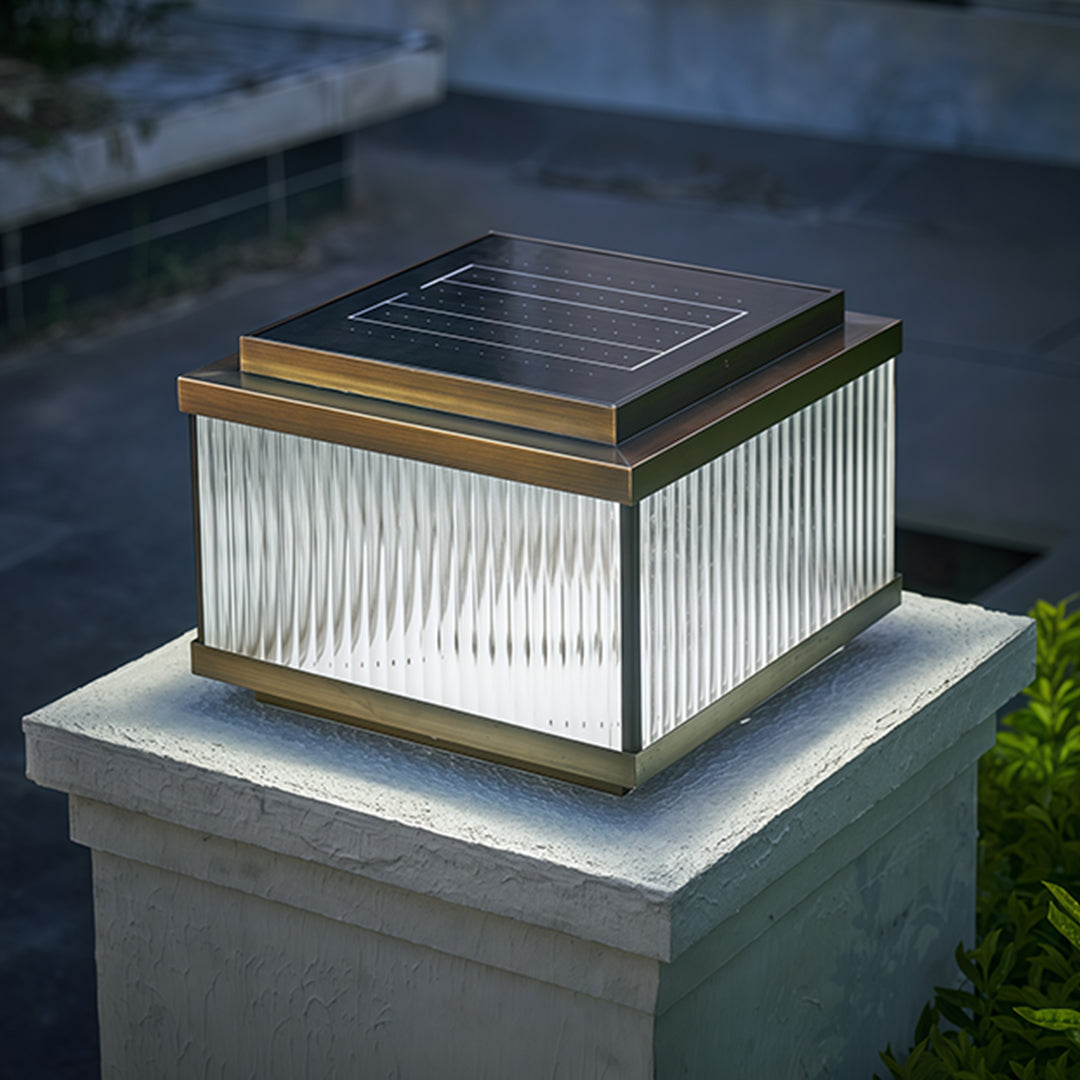 Copper pillar lights with amber glow positioned on weathered stone pillar in garden setting.