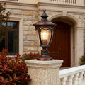 Gate pillar light glowing warmly on stone column near arched entrance with wooden door and foliage
