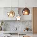 Chic glass ball pendant light set in smoke and gold over a luxury marble kitchen island desk.