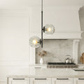 Sleek glass hanging pendant lights with water-ripple globes hanging over a luxury white island.