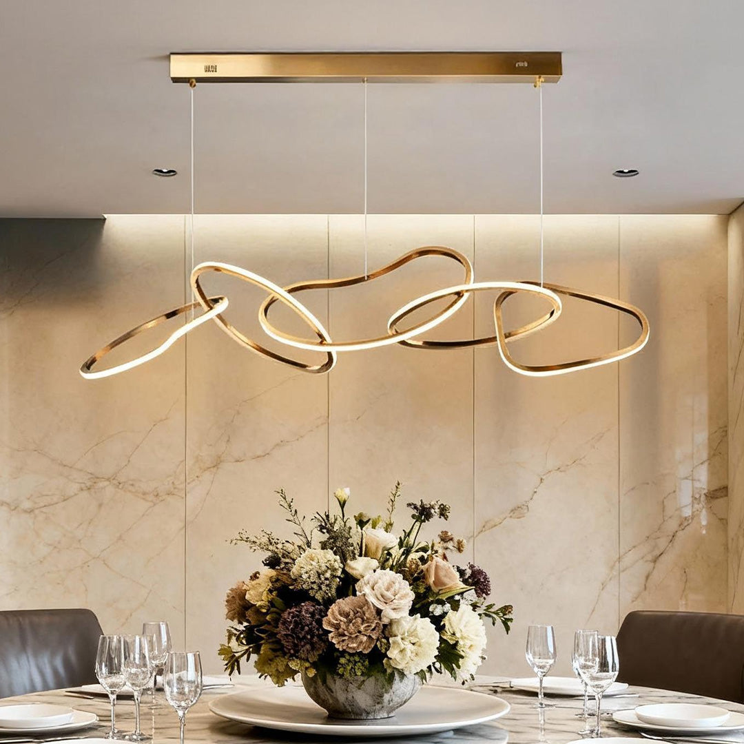 Gold circle chandelier with a modern abstract design, illuminating a luxurious dining table.