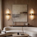 Gold and crystal wall sconces with a sleek vertical design, illuminating a modern living room.