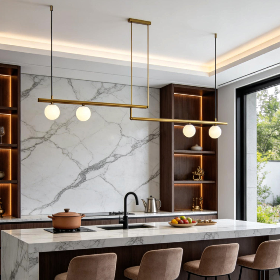 Gold linear pendant light with globe bulbs over marble kitchen counter.