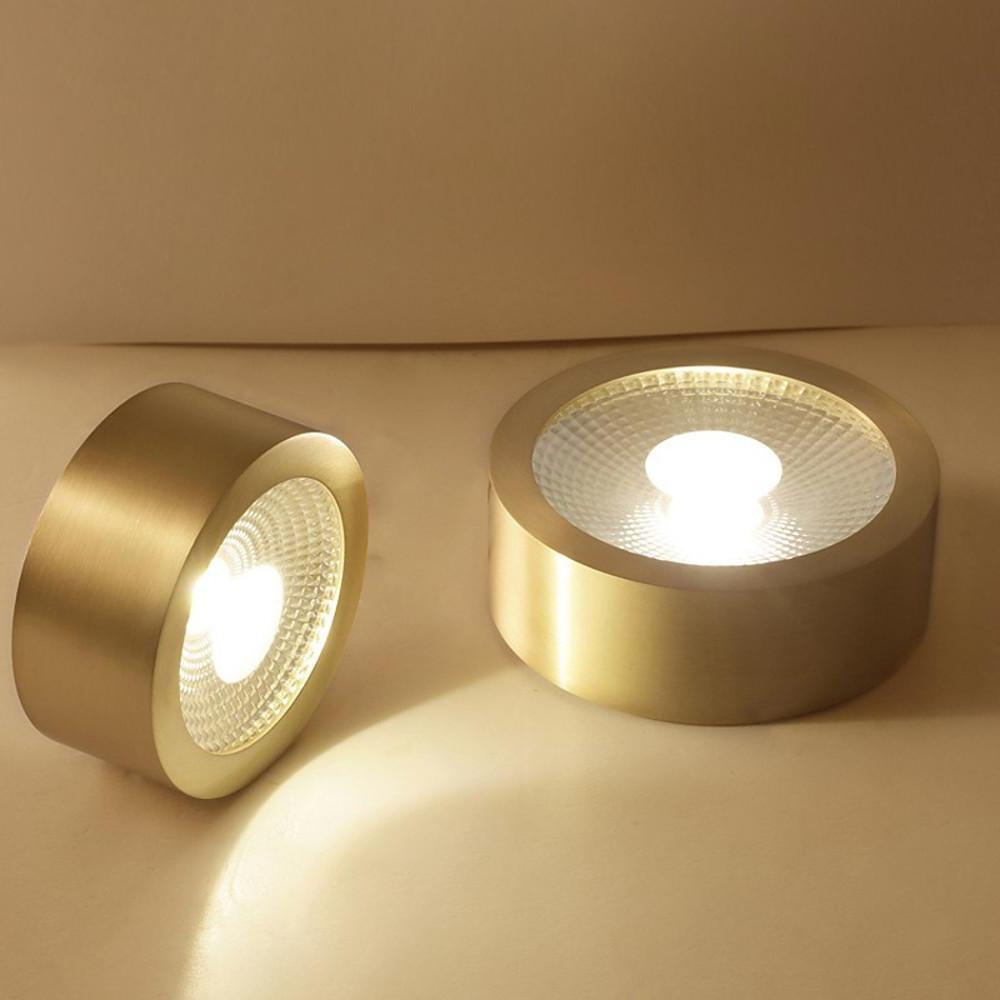 Pair of gold surface mount downlights shown on a neutral background.